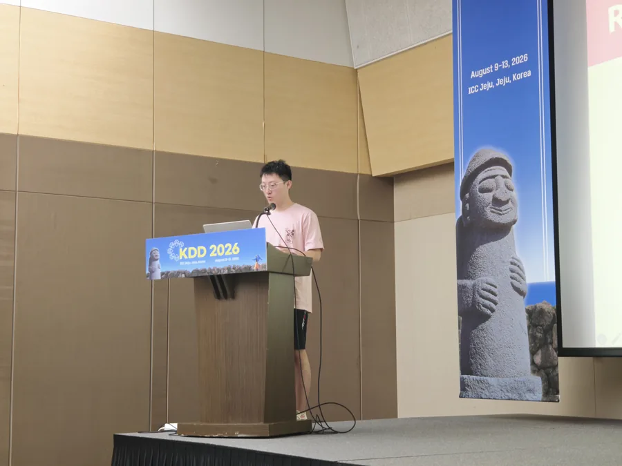 Giving a talk at a conference lectern at KDD 2026.