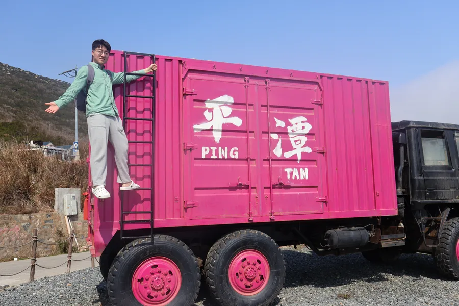 Standing beside a pink truck marked Pingtan.